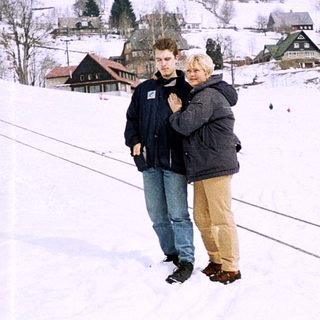 Two people embrace on snowy slope near village.