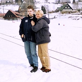 Two people embrace on snowy slope near village.