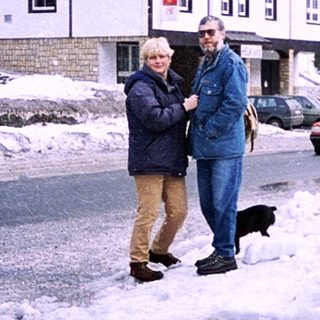 Snowy street scene with two people walking near a building.