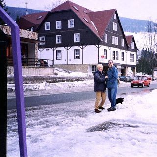 Snowy street scene with two people walking near a building.