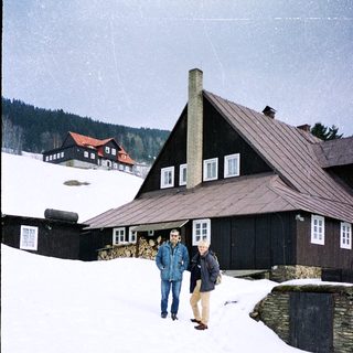 Two people standing in snowy landscape near wooden chalet.
