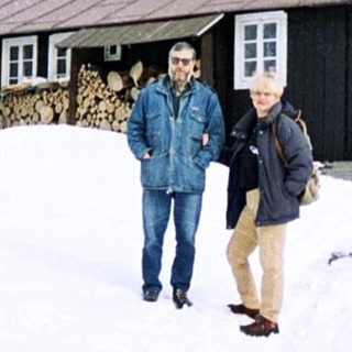 Two people standing in snowy landscape near wooden chalet.