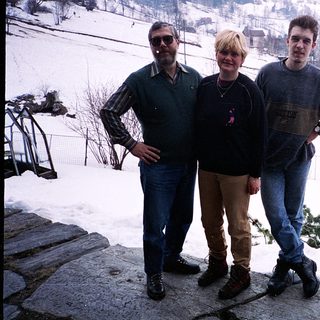 Three people posing outdoors in snowy mountainous area.