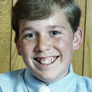 Young boy smiling in light blue dress shirt and tie.
