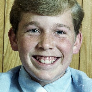 Young boy smiling in light blue dress shirt and tie.