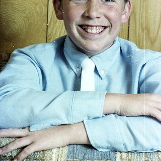 Young boy smiling in light blue dress shirt and tie.