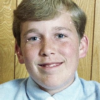 Young boy smiling in light blue shirt.