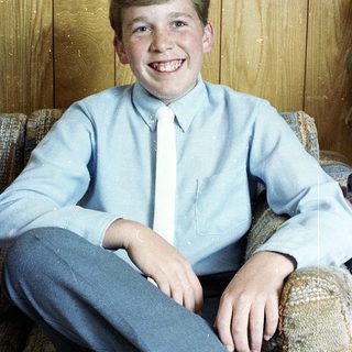 Young boy smiling in light blue shirt and tie.