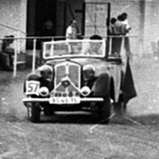 Vintage car race on dirt track with spectators.