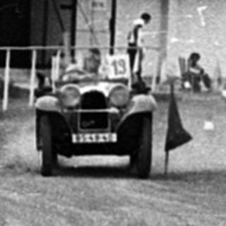 Rally car racing on dirt track with spectators.