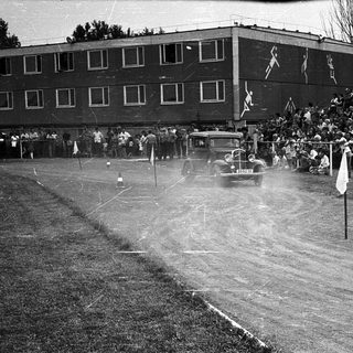 Historic car race on dirt track with spectators.