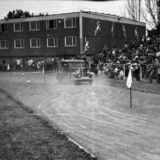Historic car race on dirt track with spectators.