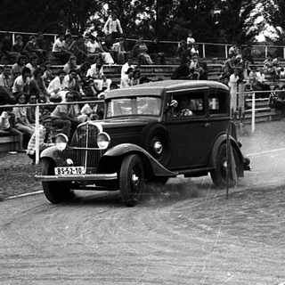 Classic car race on wet track with spectators.