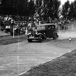 Classic car race on wet track with spectators.