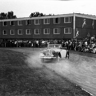 Classic car race with spectators on wet track.