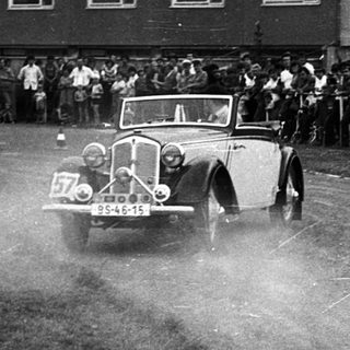 Classic car race with spectators on wet track.
