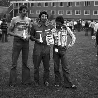 Three men posing outdoors with event badges.