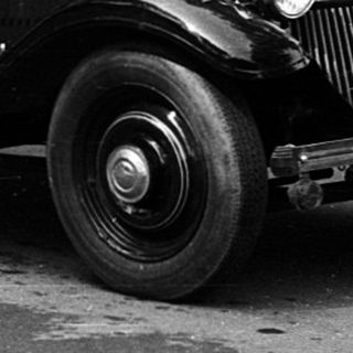 Vintage cars parked on cobblestone street with people.