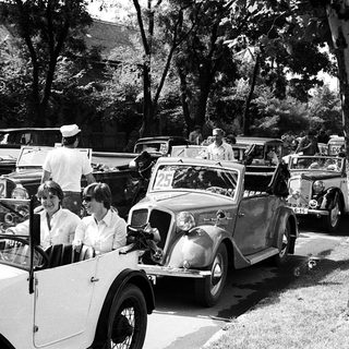 Vintage cars with people in a lined parade.