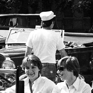 Vintage cars with people in a lined parade.