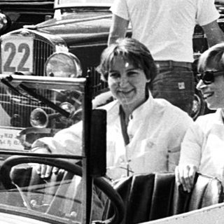 Vintage cars with people in a lined parade.