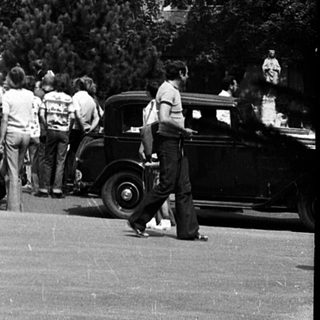 Historic church with clock tower, vintage cars, and crowd.