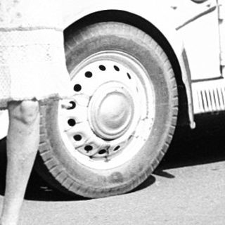 Vintage photo: man in military uniform with woman in 1940s attire near vintage cars.
