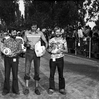 Three men holding tennis trophies at outdoor event.