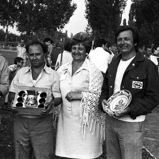 Four people holding trophies at an outdoor event.
