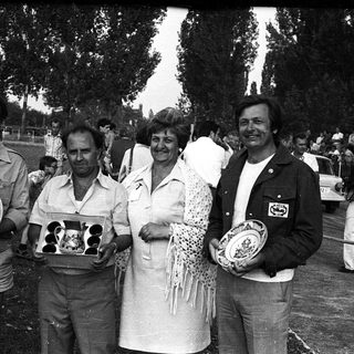 Four people holding trophies at an outdoor event.