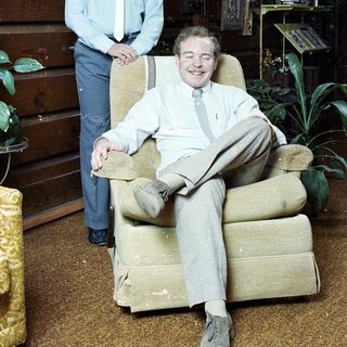 Two men in a rustic indoor setting, one seated, one standing.