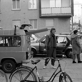 People standing with bicycles and vintage vehicles on city street.