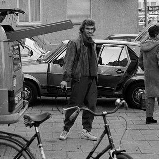 People standing with bicycles and vintage vehicles on city street.