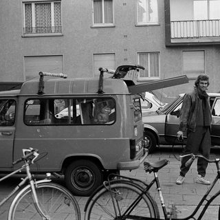 People standing with bicycles and vintage vehicles on city street.