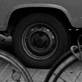 People standing with bicycles and vintage vehicles on city street.