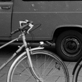 People standing with bicycles and vintage vehicles on city street.