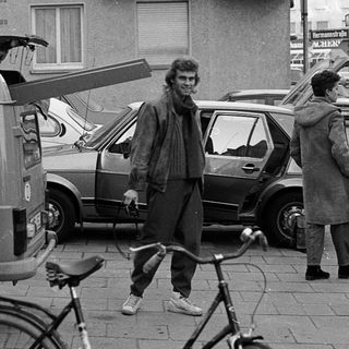 People standing with bicycles and vintage vehicles on city street.
