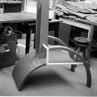 Woodshop workshop with table saw and unfinished curved furniture.