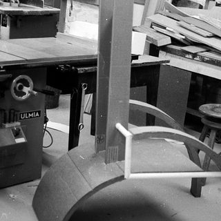 Woodshop workshop with table saw and unfinished curved furniture.