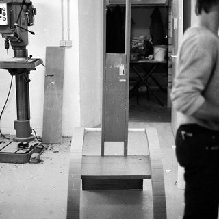 Industrial workshop with drill press and unfinished wooden bench.