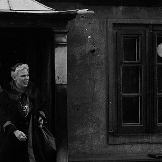 Woman in vintage coat exiting ornate building entrance.