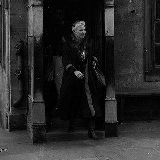 Woman in vintage coat exiting ornate building entrance.