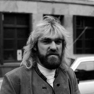 Long-haired man in urban setting, mid-1970s style.