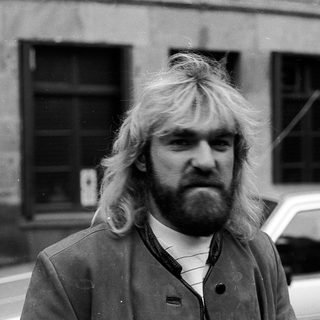 Long-haired man in urban setting, mid-1970s style.