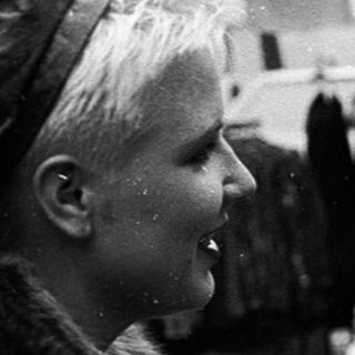 Two women examining clothing at an outdoor market stall.