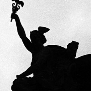 Silhouette of person raising arm with flag atop building.