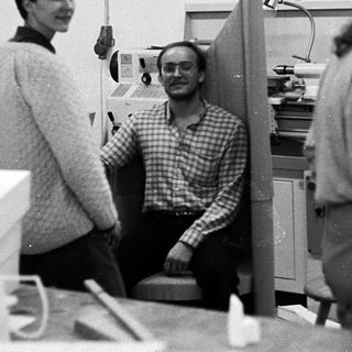Three people in an office workspace with models and equipment.