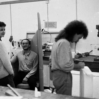 Three people in an office workspace with models and equipment.