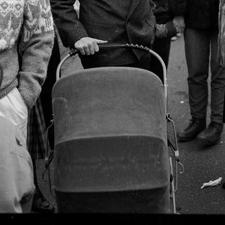 Young man pushing baby stroller in crowded outdoor setting.