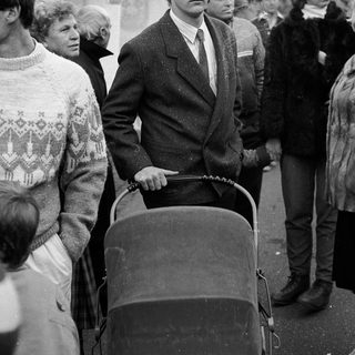 Young man pushing baby stroller in crowded outdoor setting.